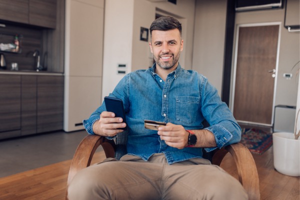 Man sitting in chair with cell phone and credit card in hand. 
